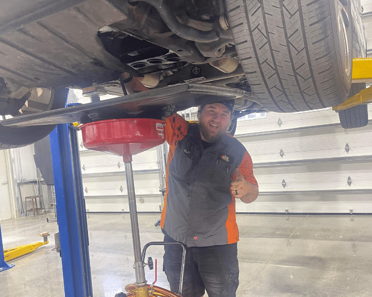 Oil Change Service in Blowing Rock, NC at L&N Performance. Image of a smiling mechanic draining oil from a lifted car to perform an oil change service.